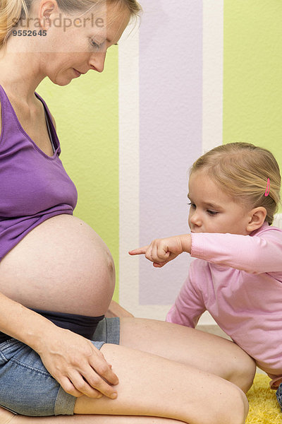 Tochter zeigt auf den Bauch einer schwangeren Frau