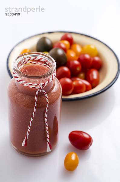 Glas Tomaten-Smoothie und Schale mit verschiedenen Mini-Tomaten