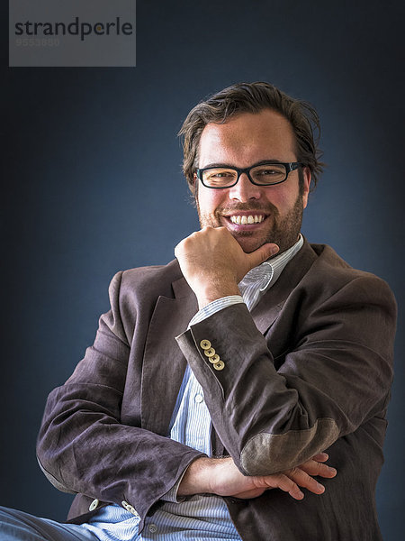 Porträt eines lächelnden Mannes mit Vollbart und Brille vor dunklem Hintergrund