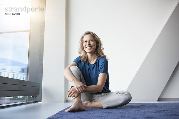 Porträt einer lächelnden reifen Frau  die in ihrer Wohnung auf dem Boden sitzt.