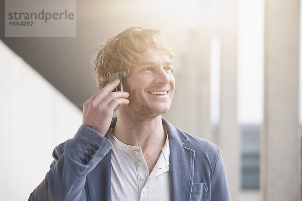 Porträt eines lächelnden Mannes beim Telefonieren mit Smartphone im Gegenlicht