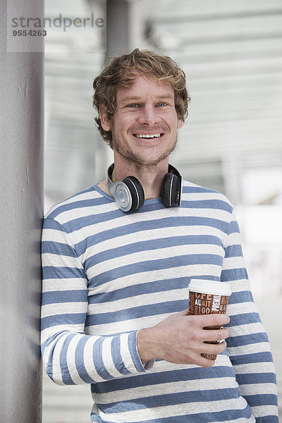Porträt eines lächelnden Mannes mit Kopfhörer und Kaffee zum Mitnehmen