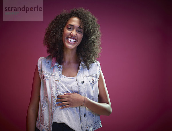 Porträt einer lachenden jungen Frau mit Afro vor rotem Hintergrund