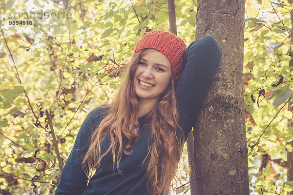 Porträt eines lachenden Teenagermädchens  das sich im Herbst an einen Baum lehnt.