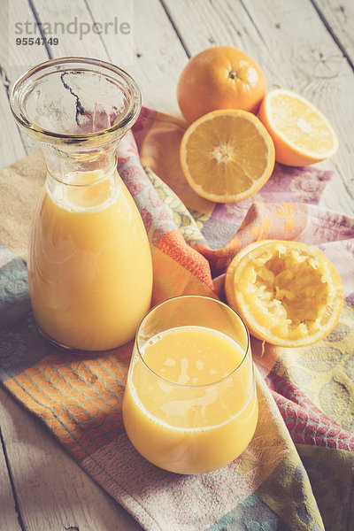 Orangen  Karaffe und Glas frisch gepresster Orangensaft auf Tuch und Holz