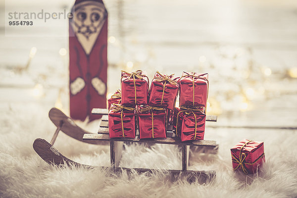 Weihnachtsmann Figur und Miniaturschlitten mit kleinen roten Weihnachtsgeschenkboxen