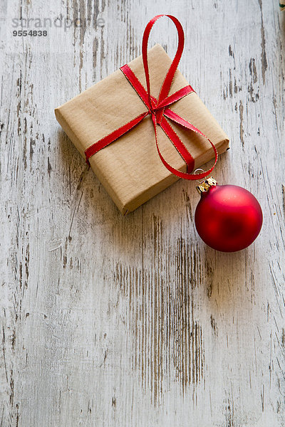 Weihnachtsgeschenk mit roter Weihnachtskugel auf Holz