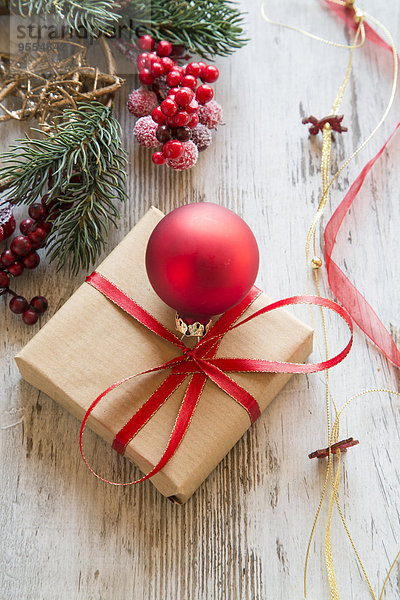 Verpacktes Weihnachtsgeschenk mit roter Weihnachtskugel auf Holz