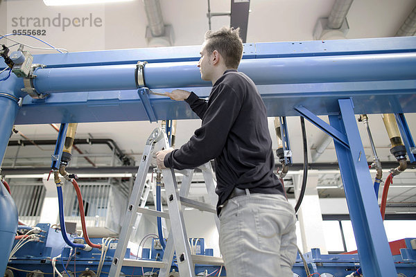 Junger Techniker beim Prüfen eines Rohres in einer Industriehalle