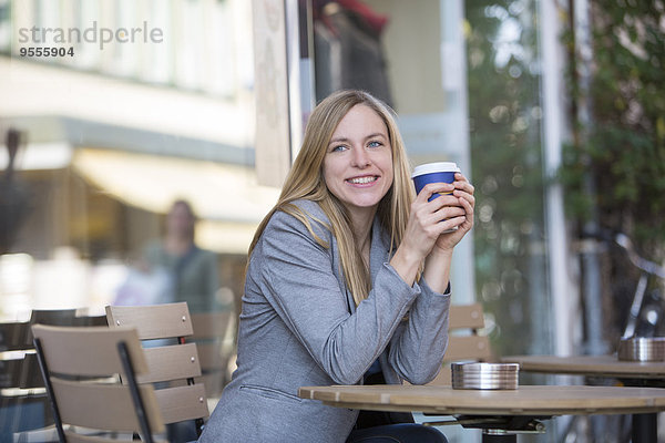 Lächelnde junge Frauen sitzen im Straßencafé mit Kaffee zum Mitnehmen