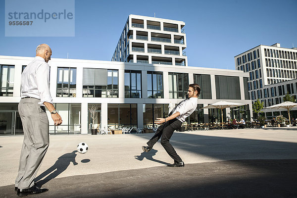 Zwei Geschäftsleute spielen Fußball im Freien.