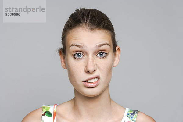 Porträt einer jungen Frau mit schmollendem Mund vor grauem Hintergrund
