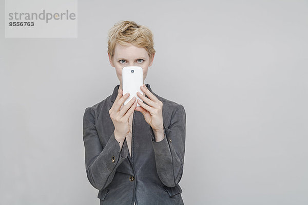 Blonde Frau beim Fotografieren mit Smartphone vor grauem Hintergrund