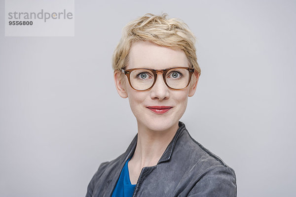 Porträt einer lächelnden blonden Frau mit Brille vor grauem Hintergrund