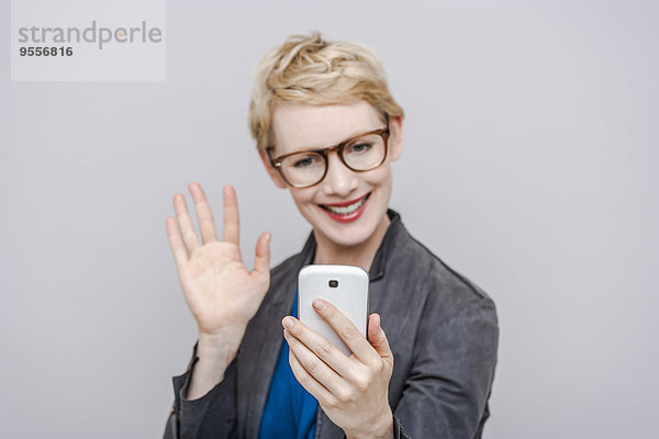 Lächelnde blonde Frau  die einen Selfie mit ihrem Smartphone nimmt.