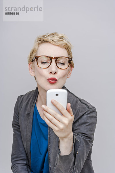 Blonde Frau mit schmollendem Mund  die einen Selfie mit ihrem Smartphone nimmt.