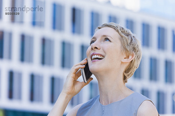 Lächelnde blonde Frau telefoniert mit Smartphone