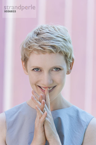 Porträt einer lächelnden blonden Frau mit Finger auf dem Mund