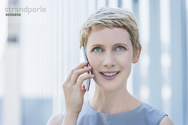 Porträt einer lächelnden blonden Frau beim Telefonieren mit dem Smartphone nach oben