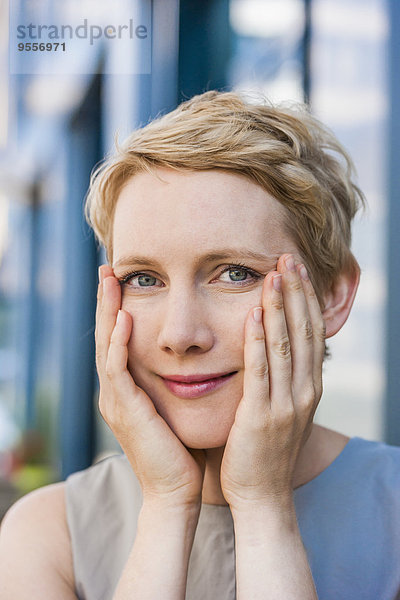 Porträt einer lächelnden blonden Frau mit Händen im Gesicht