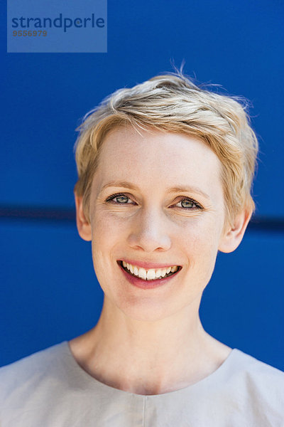 Porträt einer lächelnden blonden Frau vor blauem Hintergrund