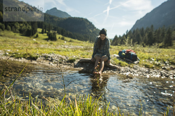 Österreich  Tirol  Tannheimer Tal  junge Wanderin entspannt am Bach