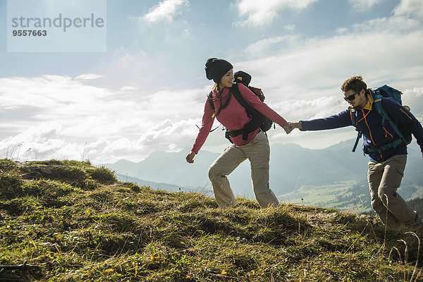 Österreich  Tirol  Tannheimer Tal  junges Paar wandert Hand in Hand auf der Alm