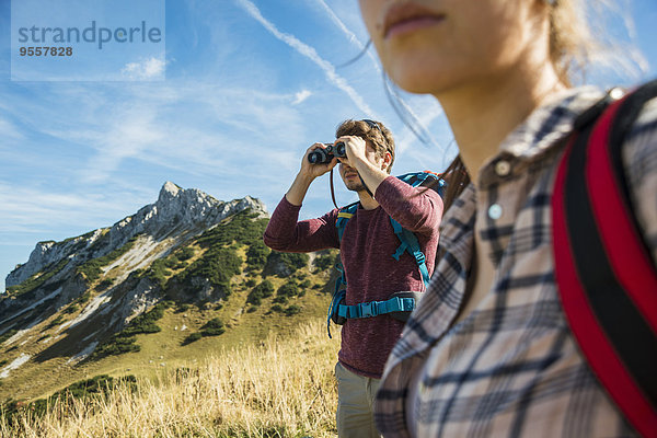 Österreich  Tirol  Tannheimer Tal  junger Mann auf Wanderung mit Blick durchs Fernglas