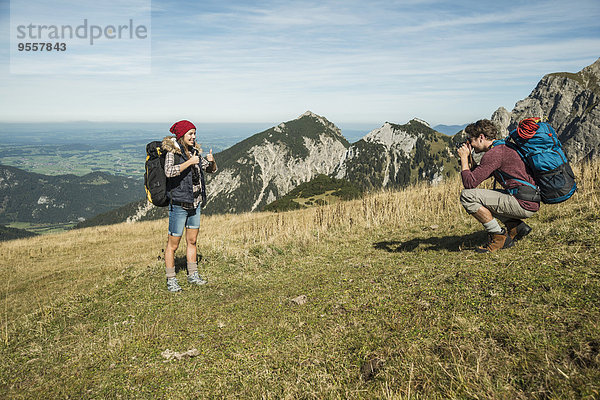 Österreich  Tirol  Tannheimer Tal  junger Mann fotografiert Freundin auf der Alm