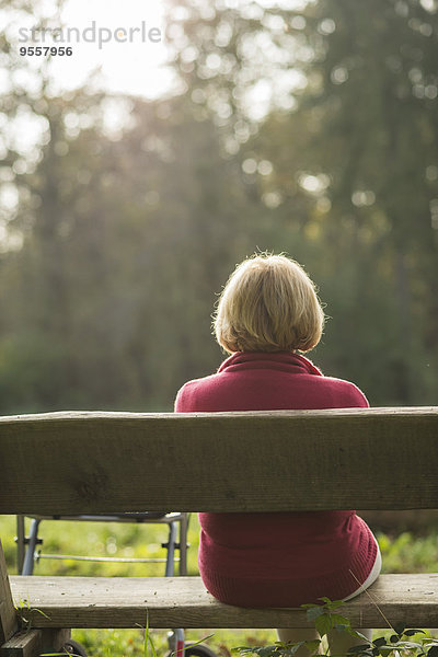 Seniorin auf einer Parkbank sitzend  Rückansicht