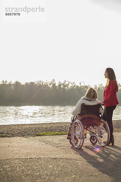 Enkelin  die ihrer Großmutter im Rollstuhl assistiert