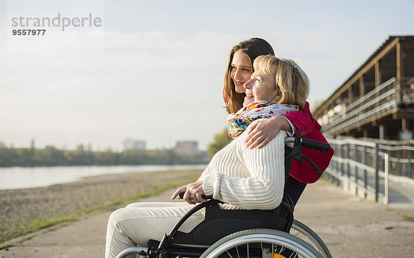 Enkelin  die ihre Großmutter im Rollstuhl umarmt.