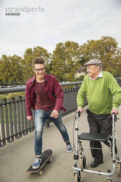 Fröhlicher Senior mit Rollator und erwachsenem Enkel mit Skateboard