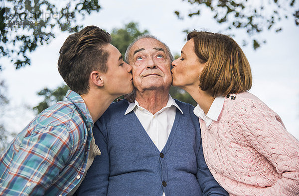Enkel und Tochter küssen die Wange des älteren Mannes
