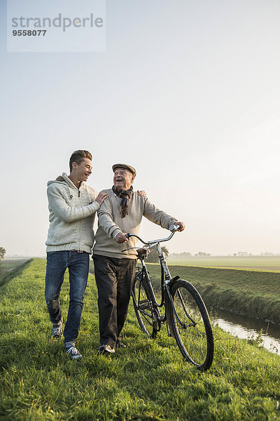 Senior Mann und Enkel in ländlicher Landschaft mit Fahrrad