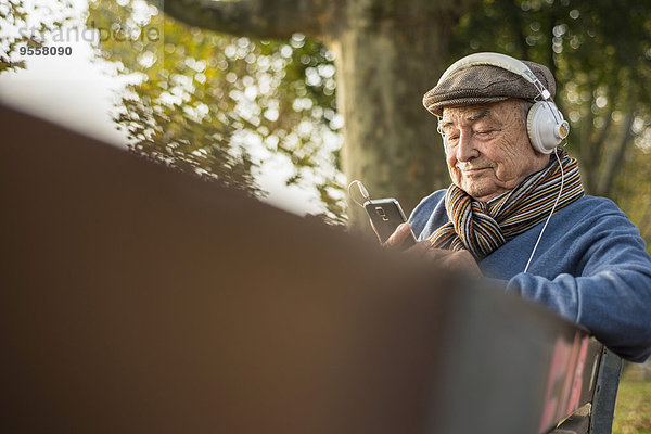 Senior auf Parkbank mit Handy und Kopfhörer