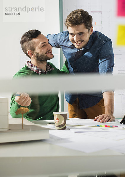 Zwei lächelnde junge Männer im Büro mit Architekturmodell