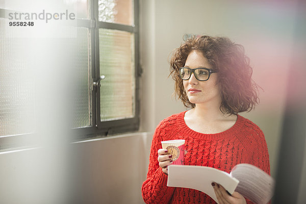 Junge Frau mit Dokument und Kaffee am Fenster