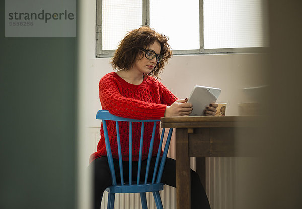 Junge Frau mit digitalem Tablett am Tisch sitzend