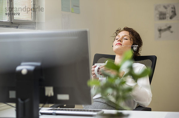 Junge Frau im Büro mit zurücklehnendem Headset