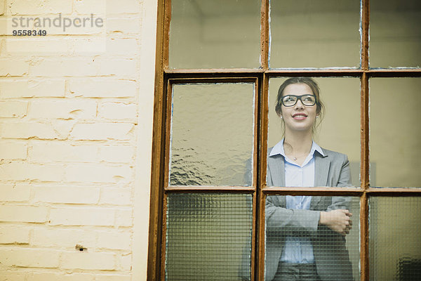 Lächelnde junge Geschäftsfrau schaut aus dem Fenster