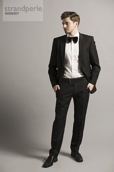 Junger Mann mit den Händen in den Taschen in schwarzem Anzug  weißem Hemd und Schleife.