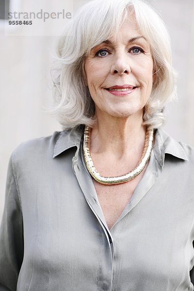 Porträt der lächelnden weißhaarigen Seniorin mit Bluse und Halskette