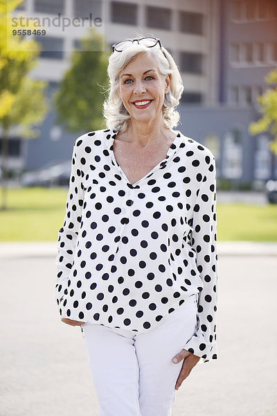 Porträt der lächelnden Seniorin in weißer Bluse mit schwarzen Punkten