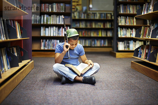 Junge mit Helm und Waffenlesebuch in der Bibliothek
