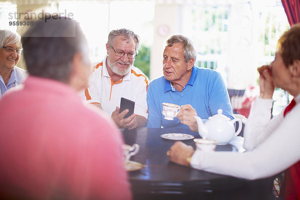 Senior Mann zeigt Smartphone einem Freund am Couchtisch