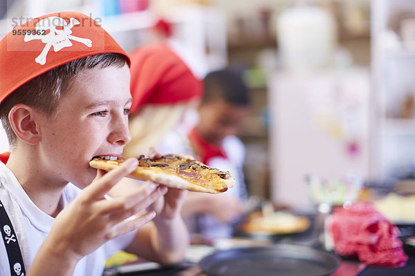 Junge als Pirat verkleidet  der auf einer Party Pizza isst.