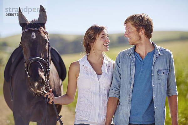 Ein junges Paar  das mit einem Pferd auf dem Land spazieren geht.