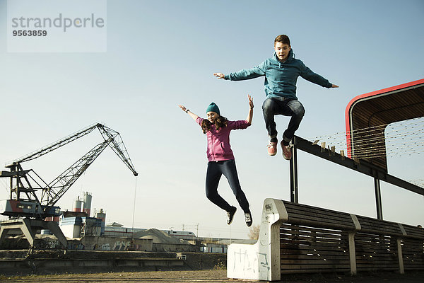 Außenaufnahme Jugendlicher Junge - Person über springen Sitzbank Bank Mädchen Industriegebiet freie Natur