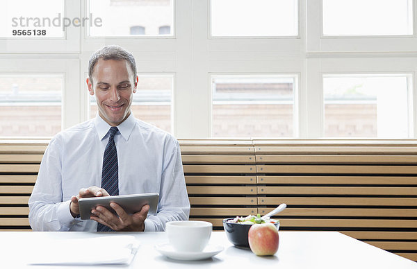 Ein Geschäftsmann  der in seiner Mittagspause ein digitales Tablett benutzt.